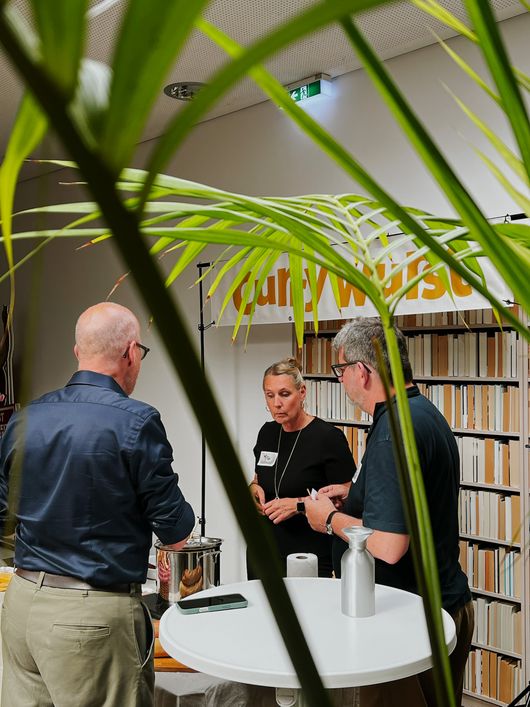 Drei Gäste im Networking-Gespräch, Bücherwand mit Currywurst-Schriftzug im Hintergrund