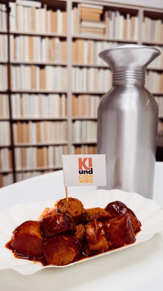 Currywurst mit KI-und-Currywurst-Fähnchen im Büchersaal des Heine Hauses