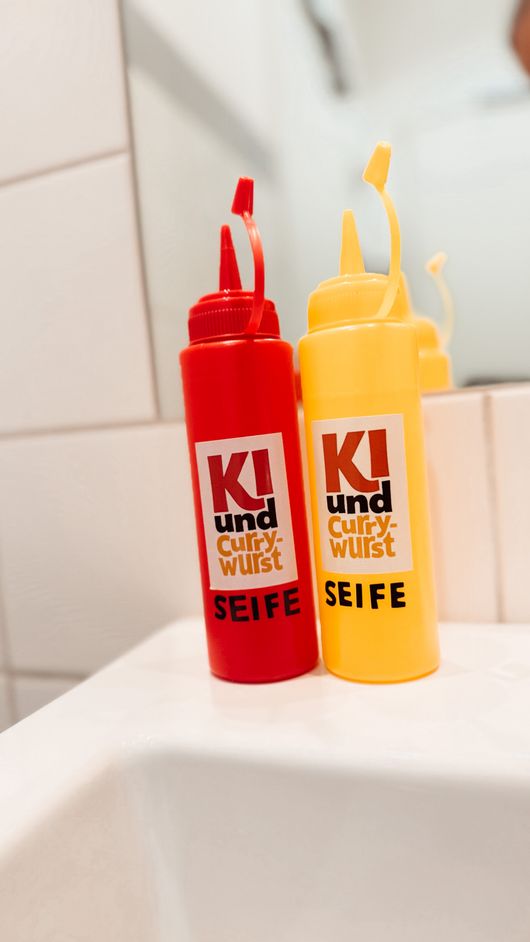 Gebrandete Seifenflaschen in Rot und Gelb mit KI-und-Currywurst-Logo