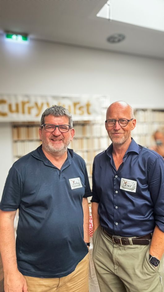 Zwei Gäste beim Networking, Currywurst-Schriftzug im Hintergrund
